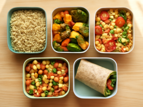 Vijf gevulde meal prep lunchboxen met gezonde ingrediënten op een houten aanrecht